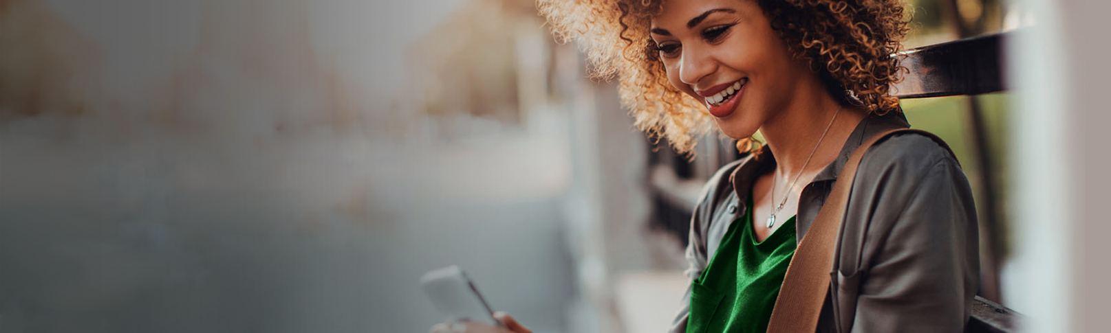 girl smiling while sitting on a bench and  looking at her phone