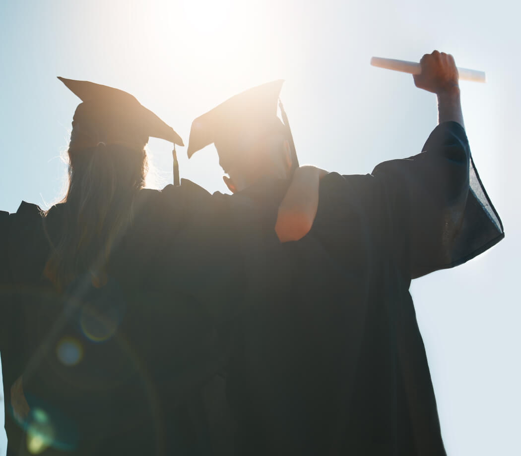 Two graduates celebrate with arms raised 