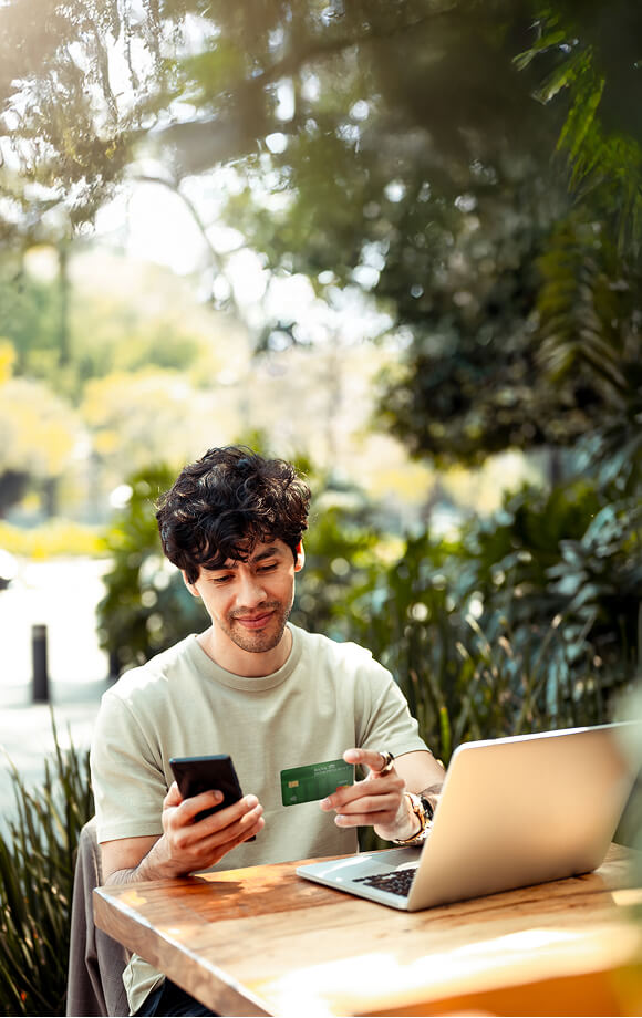 Young man holding mobile phone and debit card while sitting in front of computer